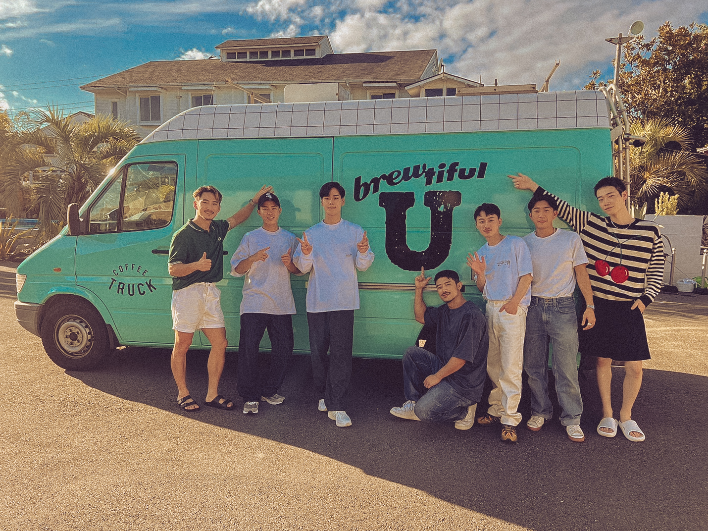 The boys of Netflix’s The Boyfriend gather around the show’s turquoise coffee truck in a warm, sunlit group portrait.