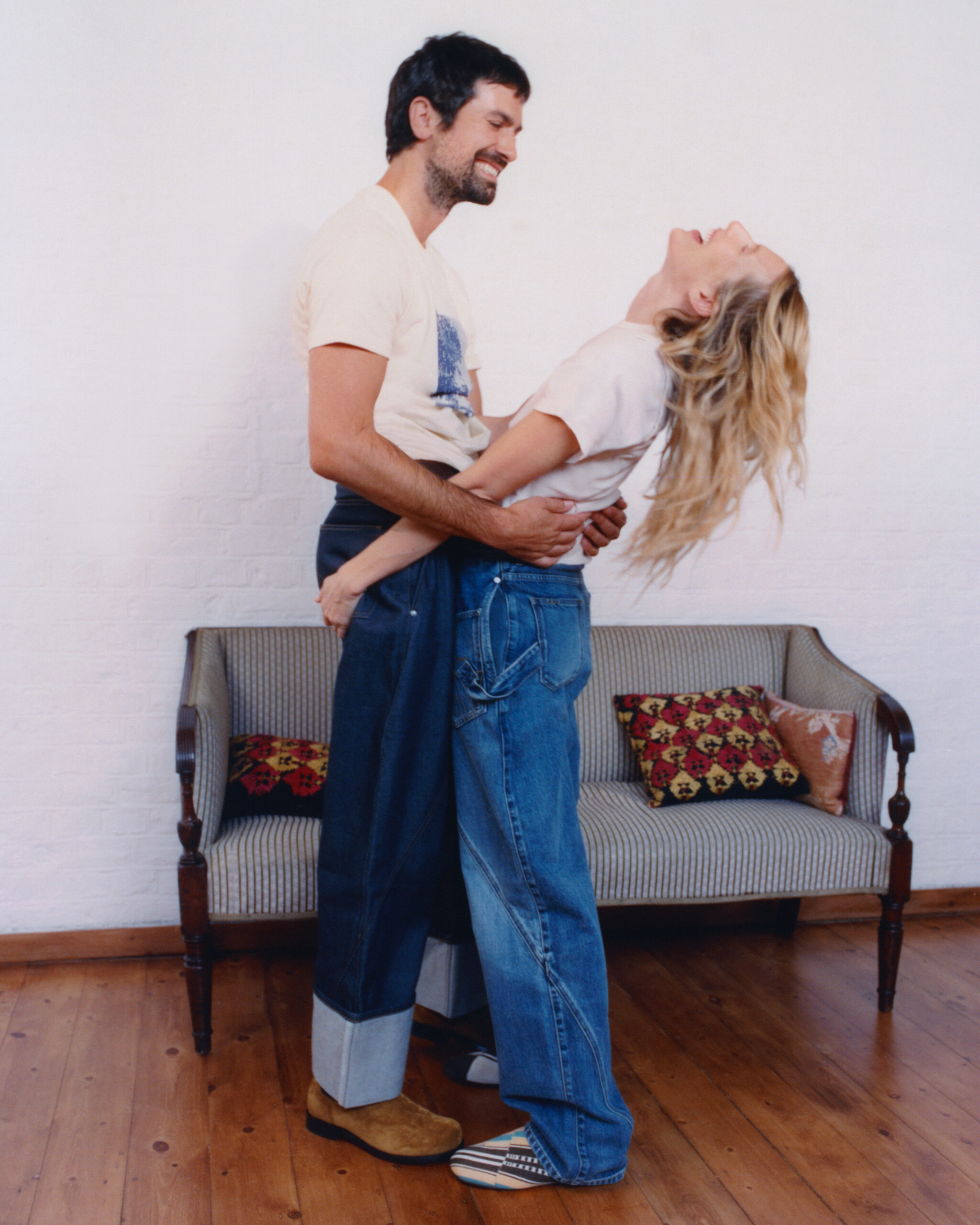 Dree Hemingway thrown back laughing in Nick Delli Santi's arms, both in JW Anderson Twisted Denim