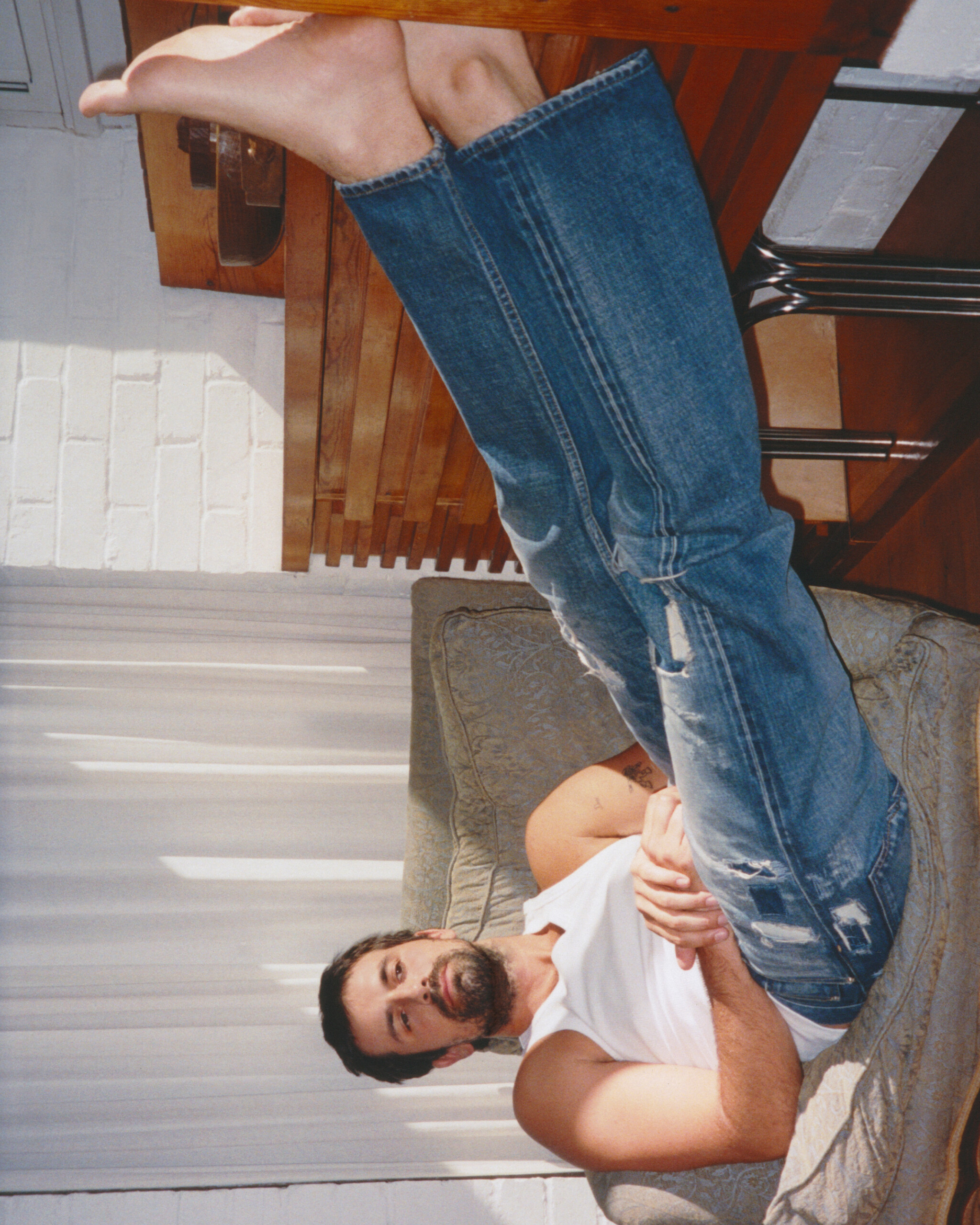 Nick Delli Santi lying across a settee in JW Anderson Twisted Denim jeans