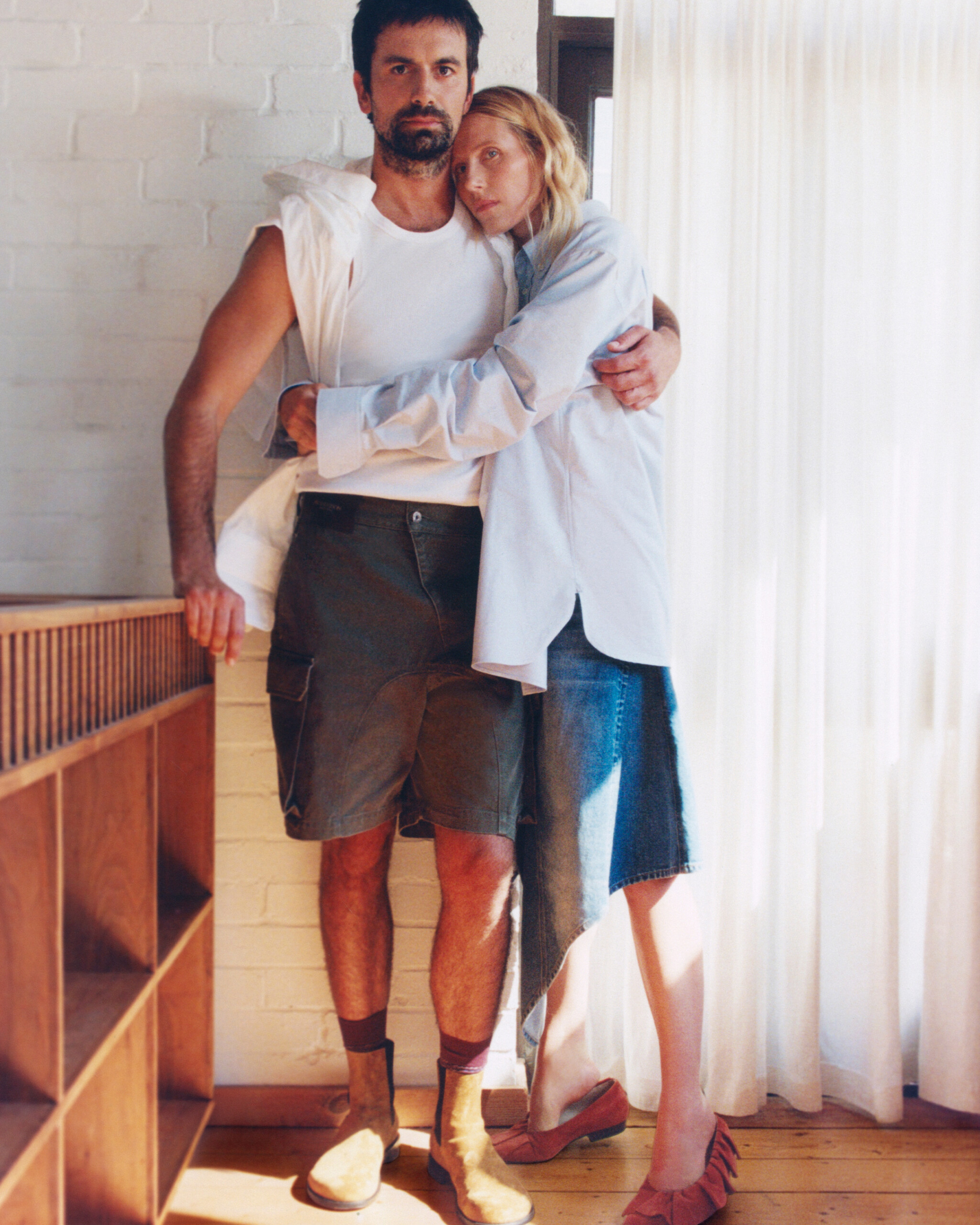 Dree Hemingway and Nick Delli Santi embracing by a curtained window in JW Anderson