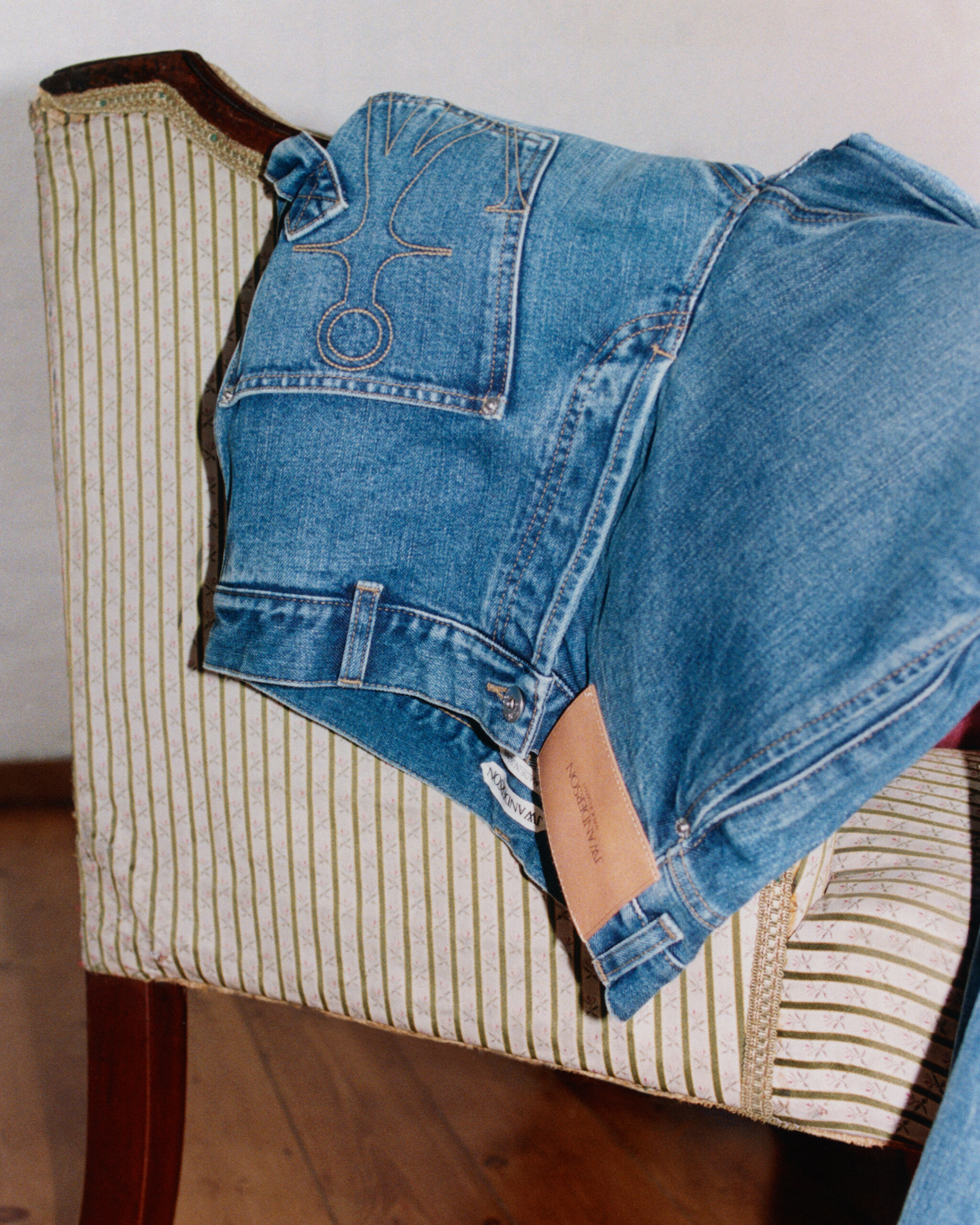 JW Anderson Twisted Denim jeans draped over a striped antique chair